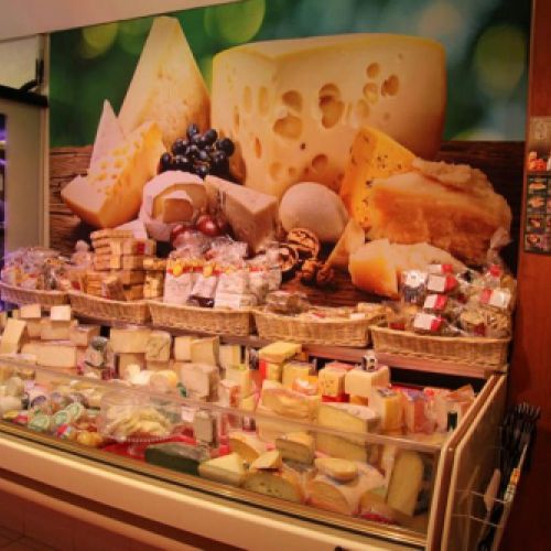 Expositor amb formatges i vinil decoratiu a paret a l'interior de la botiga vist des de la dreta