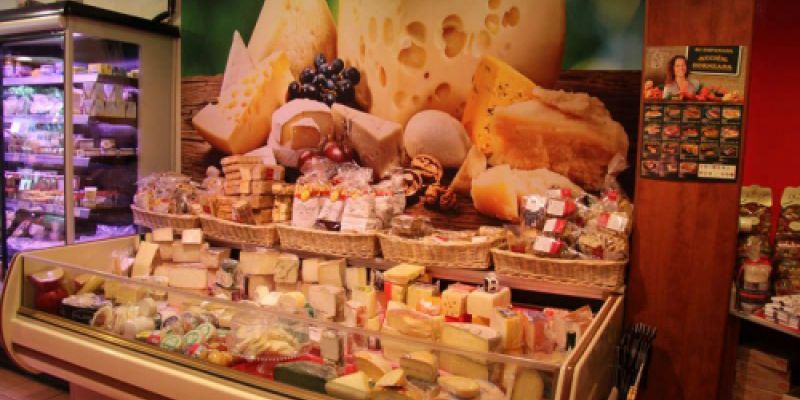 Expositor con quesos y vinilo decorativo en pared en el interior de la tienda visto desde la derecha